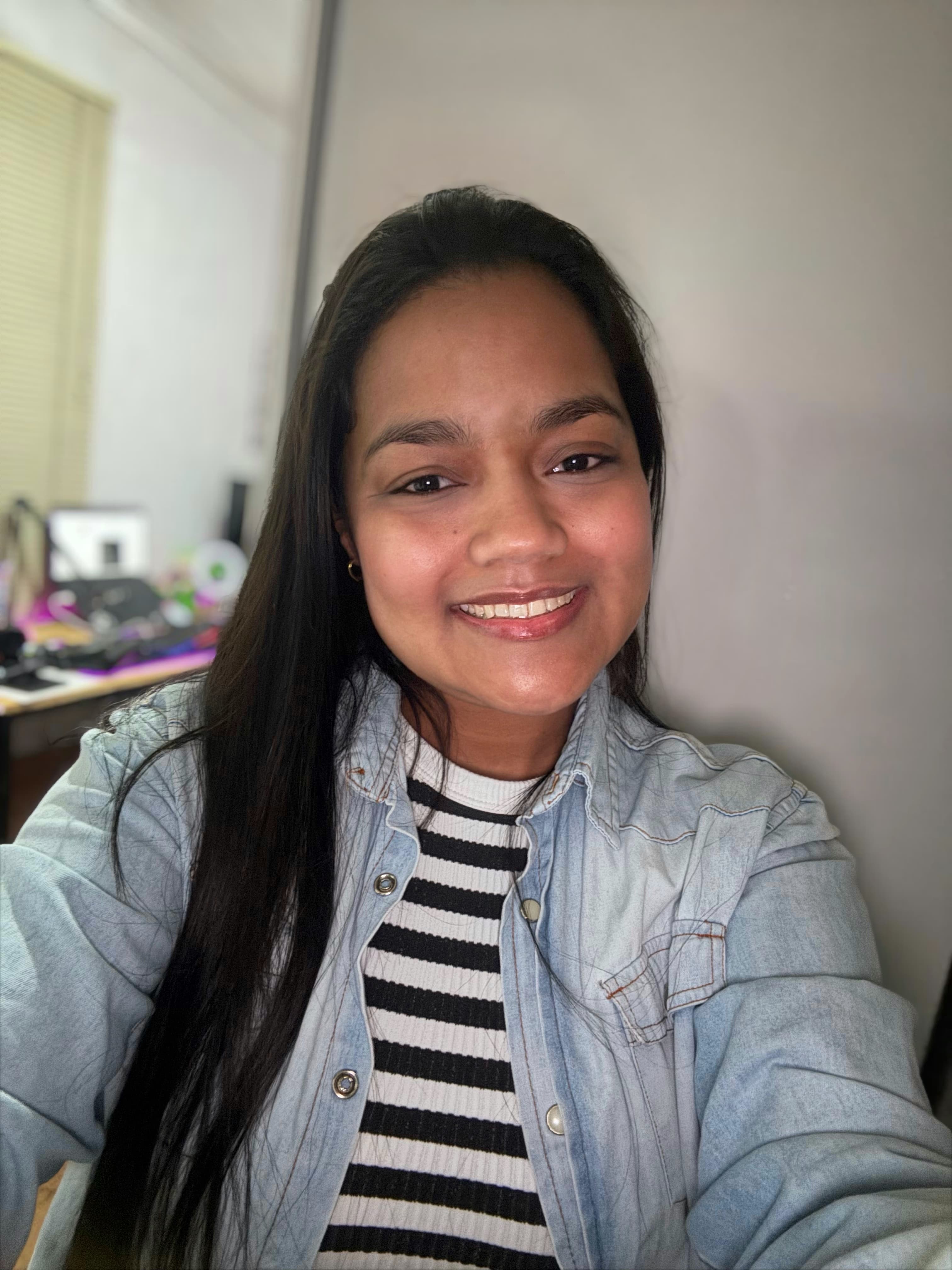 Retrato de Caroline Paier, uma mulher negra sorrindo levemente para a câmera. Ela veste uma camiseta listrada sob uma jaqueta jeans.